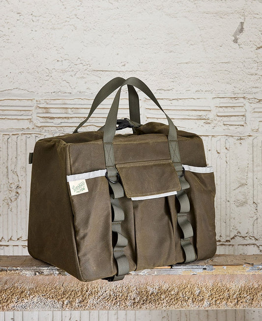 A Olive duffel bag with two carry straps, a front flap pocket with hook and loop closure, and additional slip pockets. It is placed against a textured background. Garner and Tow Duffel Slate