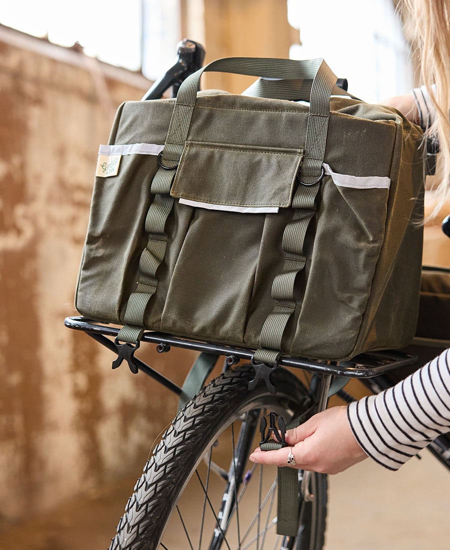 an olive duffel bag sitting on the front rack of a black bike