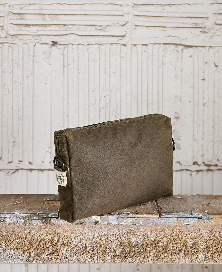 An Olive fabric pouch with a zippered closure, placed on a wooden surface against a white textured background.