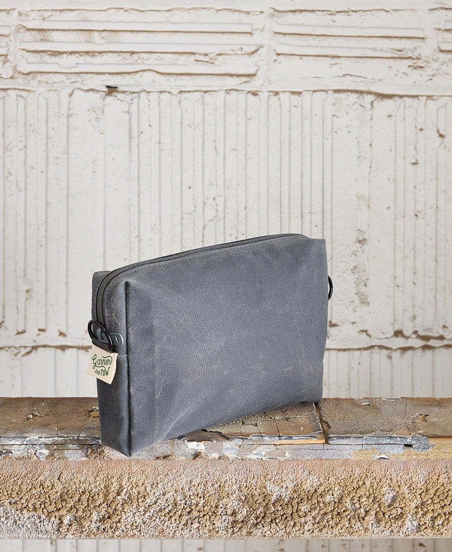 A gray fabric pouch with a zippered closure, placed on a wooden surface against a white textured background.