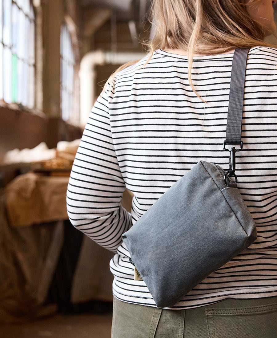 Grey fabric pouch used a sling over ther shoulder on the back of a women