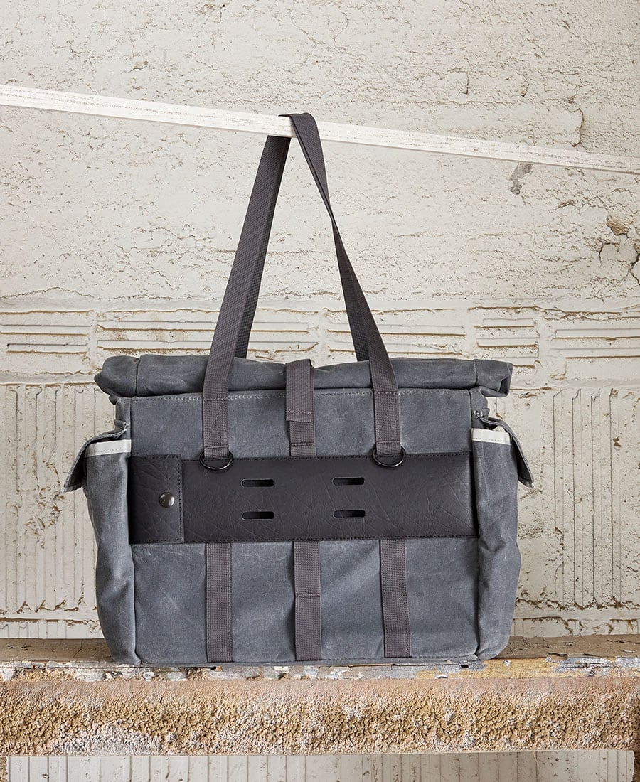 A gray tote bag with multiple external pockets and shoulder straps, displayed against an indoor backdrop.