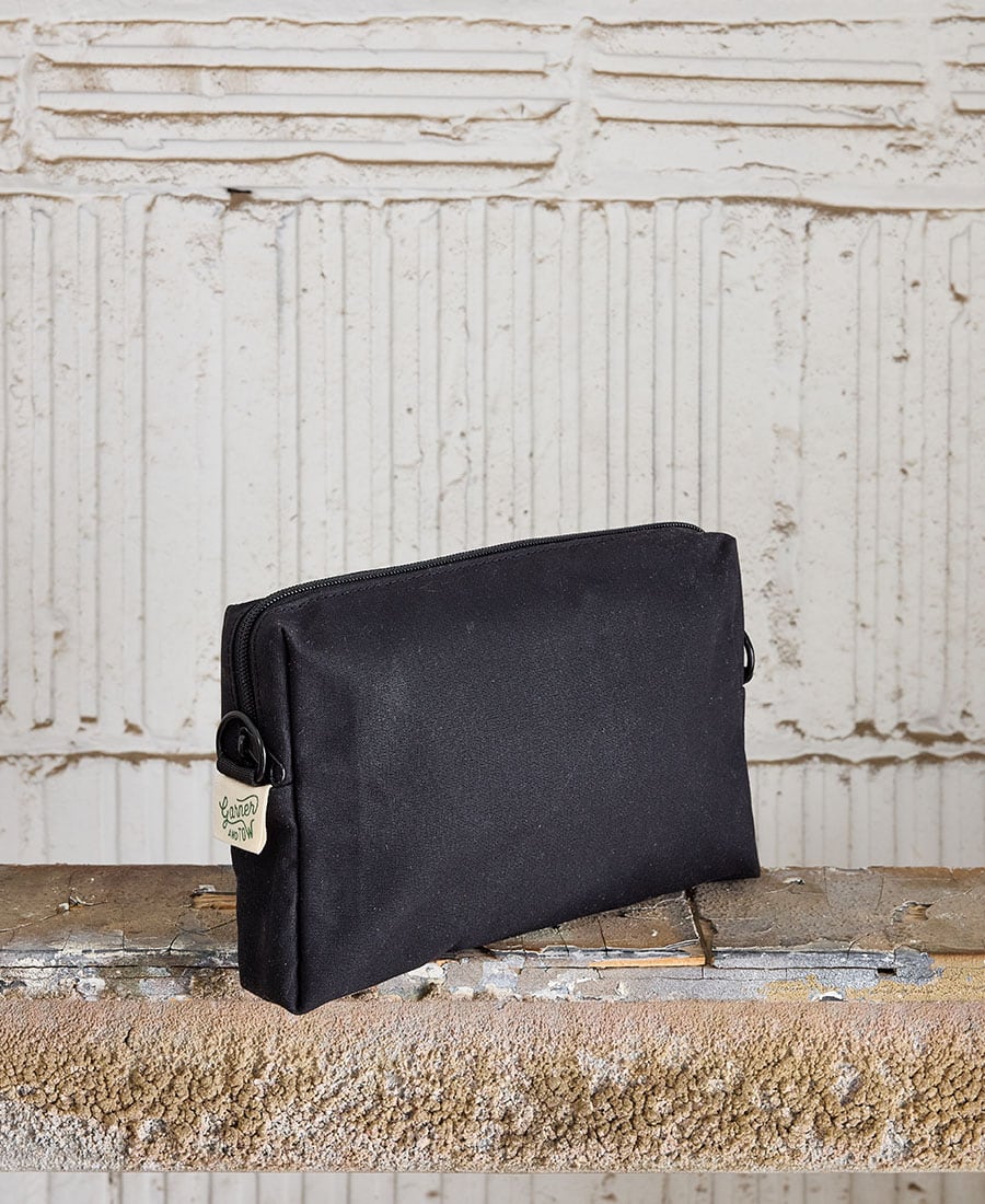 A black fabric pouch with a zippered closure, placed on a wooden surface against a white textured background.